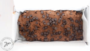 Chocolate chips sprinkled over raw Chocolate Pumpkin Bread dough in a parchment lined loaf pan.