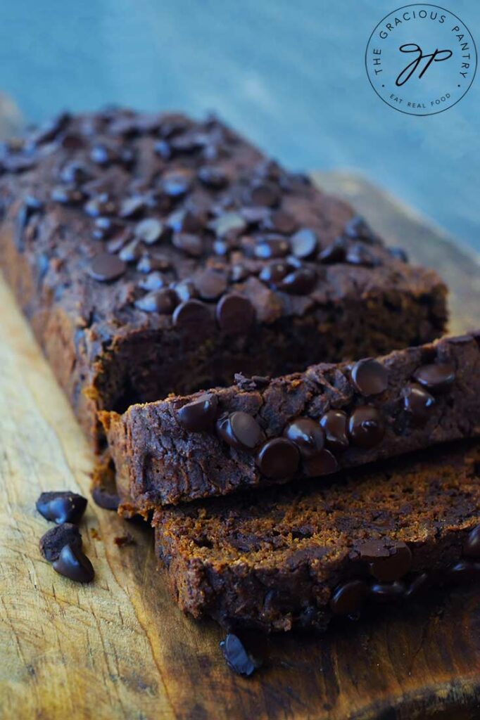 A side view of a Chocolate Pumpkin Bread loaf sitting on a cutting board with two slices laying at the front.