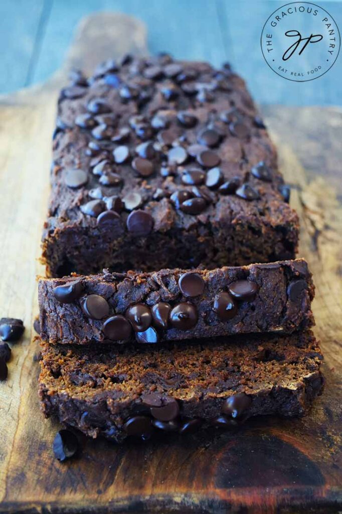 A head on view of a loaf of Chocolate Pumpkin Bread sitting on a cutting board with two slices cut at the front.