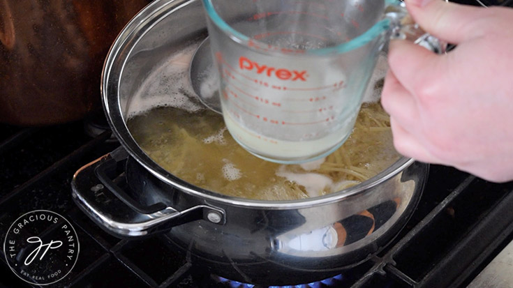 Ladling hot pasta water into a measuring cup for carbonara sauce.