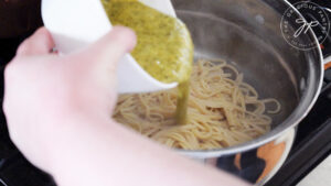 Pouring carbonara sauce over cooked pasta in a stainless steel pot.