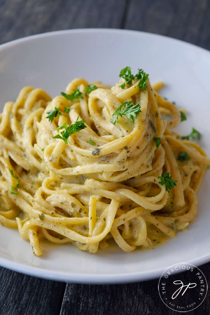 A closeup of a white pasta bowl filled with a pile of Dairy-Free Carbonara and garnished with fresh, chopped parsley.