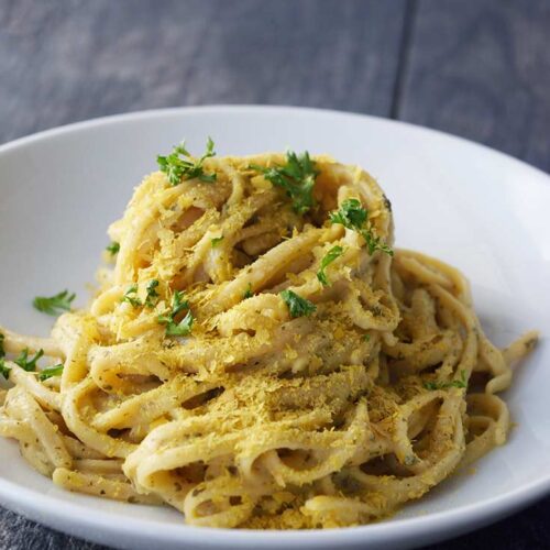 A white bowl with Dairy-Free Carbonara that has been topped with fresh parsley and sprinkled with nutritional yeast.