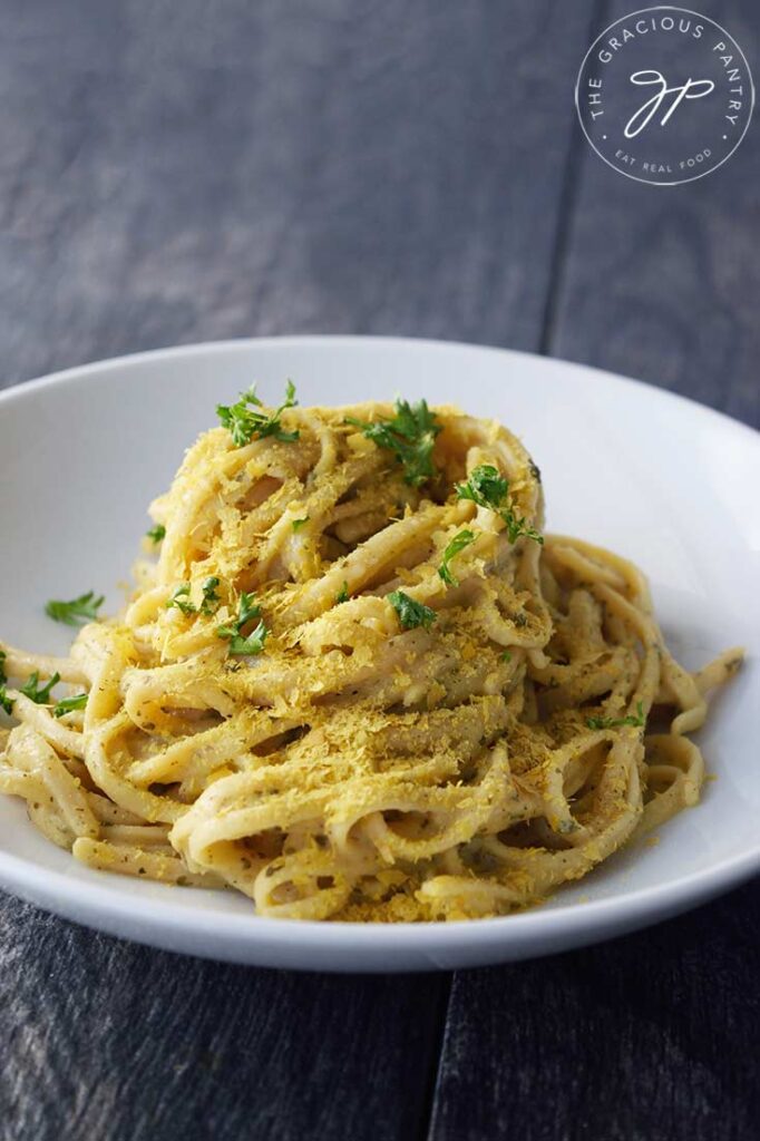 A white bowl with Dairy-Free Carbonara that has been topped with fresh parsley and sprinkled with nutritional yeast.