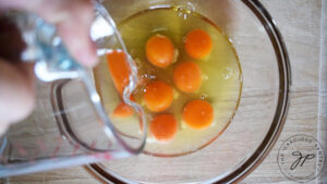 Water being poured into a mixing bowl of eggs.