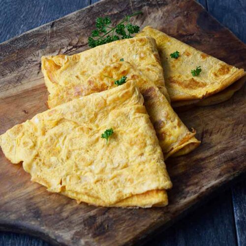 Folded egg wraps on a cutting board sprinkled with fresh, chopped parsley.