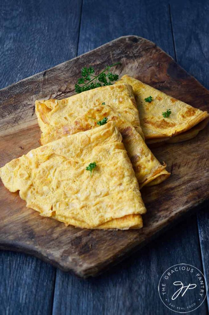 Folded egg wraps on a cutting board sprinkled with fresh, chopped parsley.