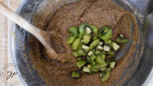 Chopped kiwi being folded into a batter in a mixing bowl.