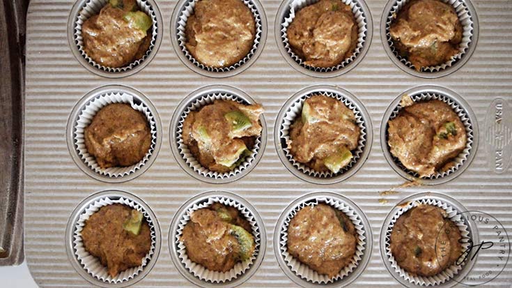 a muffin pan with liners filled with kiwi muffin batter.