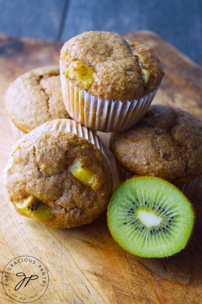 Muffins stacked on a cutting board with half a kiwi sitting next to them.