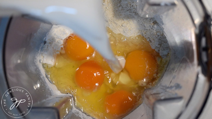 Milk being poured into a blender that already has eggs, flour and starch in it.