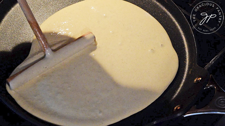 Spreading crepe batter over a pan with a crepe spreader.