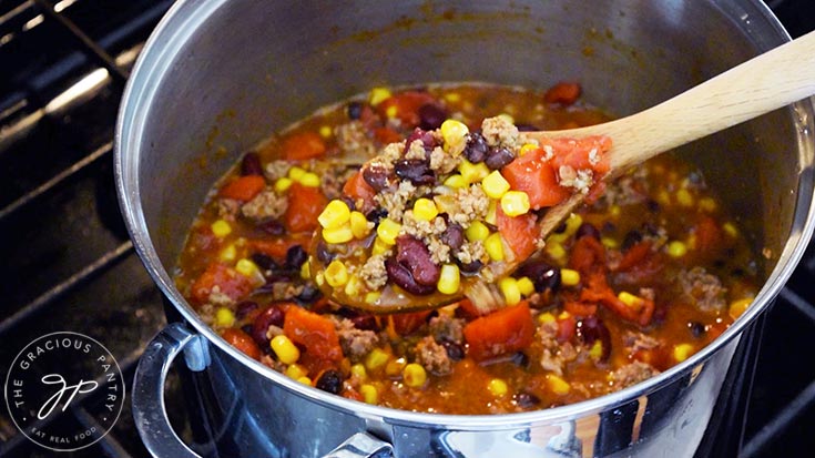 A wooden spoon lifts some 2 Bean Turkey Chili towards the camera out of a stock pot.