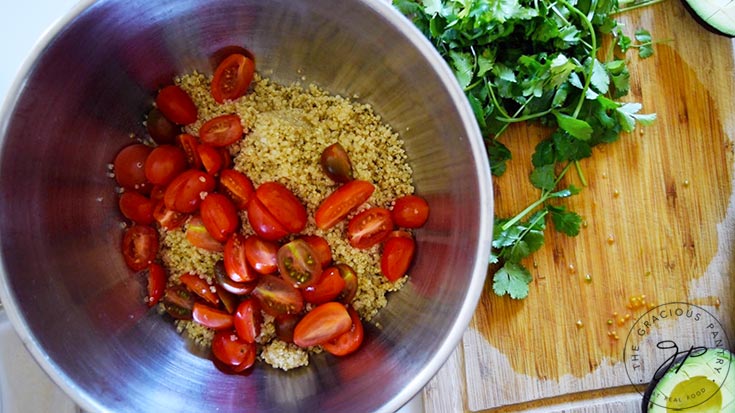 Sliced grape tomatoes added to quinoa in a large mixing bowl.
