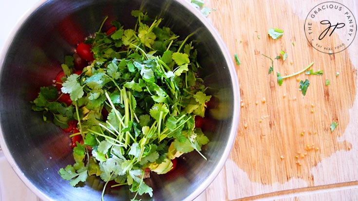 Fresh, chopped cilantro added to a mixing bowl filled with quinoa, sliced grape tomatoes and avocado chunks.