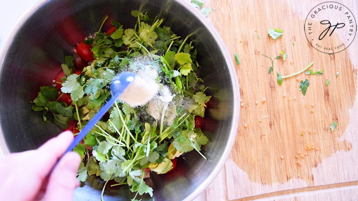 Adding spices to a mixing bowl filled with Avocado Quinoa Salad Recipe ingredients.