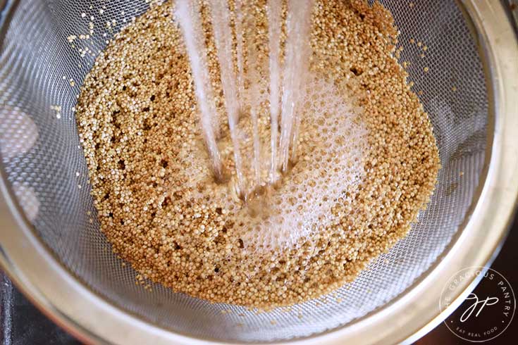 Rinsing quinoa in a metal, mesh strainer.