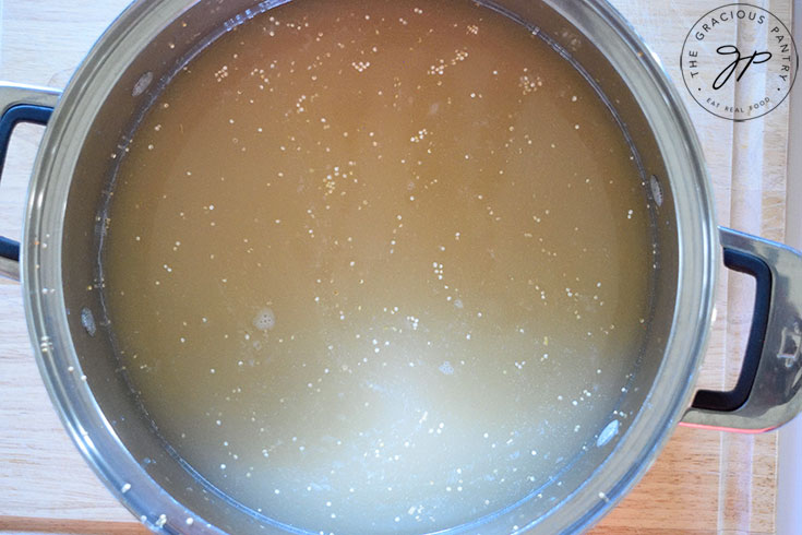 Quinoa and broth in a stainless steel pot.