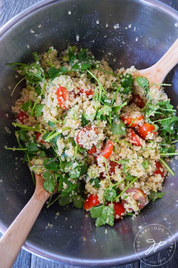 A mixing bowl with just mixed Avocado Quinoa Salad. Wooden spoons rest on the sides of the bowl.