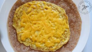 The egg pancake with cheese on a whole wheat tortilla sitting on a white plate.