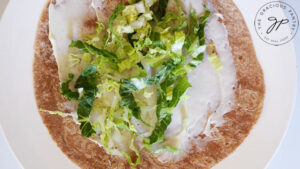 Lettuce spread over mayonnaise on a whole wheat tortilla.