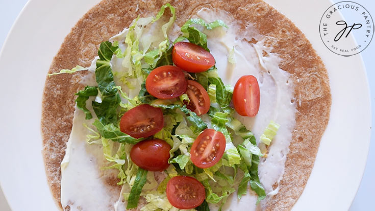 Halved grape tomatoes laying on lettuce and mayonnaise on a whole wheat tortilla.