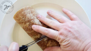 Cutting a BLT Wrap in half on a white plate.