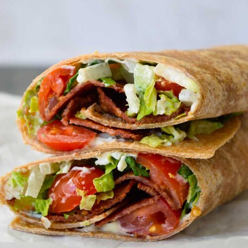 A view of the cut sides of a BLT wrap which have been stacked up on a piece of parchment paper.
