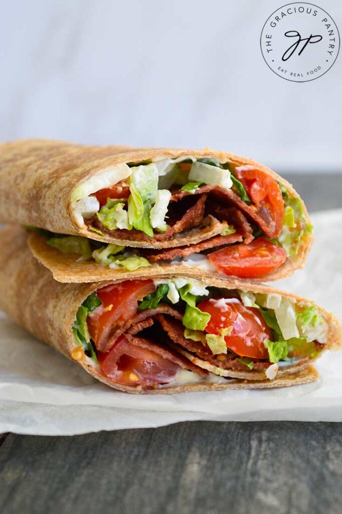 A side angle of a cut BLT Wrap laying stacked on a piece of parchment.