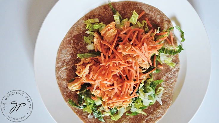 A layer of grated carrots added over the buffalo chicken and lettuce on a tortilla.