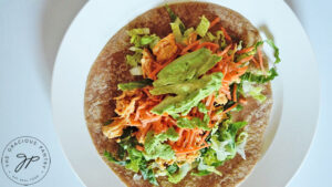 Avocado placed over the carrots and buffalo chicken on a tortilla with lettuce.