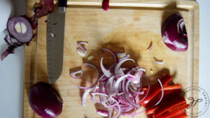 Sliced red bell peppers and red onions on a cutting board.