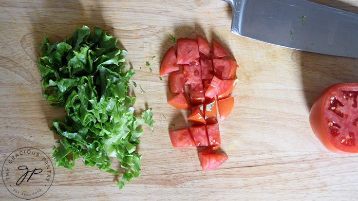 Sliced lettuce and chopped tomatoes on a cutting board.