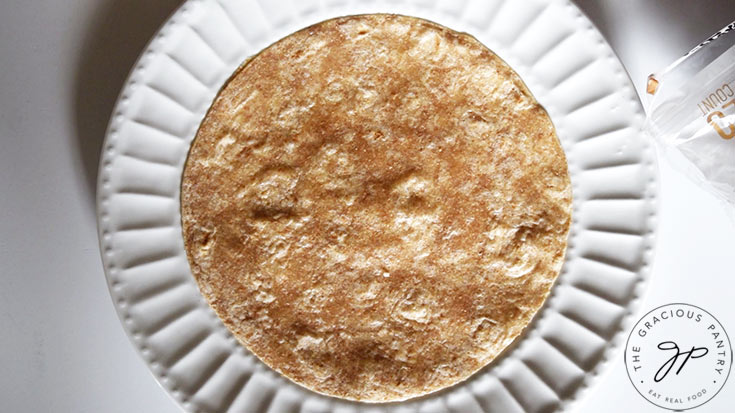 A whole grain tortilla laying on a white plate.
