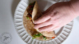 Rolling up a Cajun Chicken Wrap on a white plate.