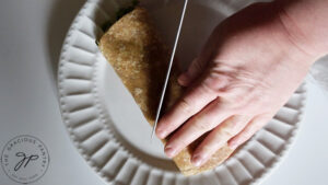 Slicing a Cajun Chicken Wrap in half on a white plate.