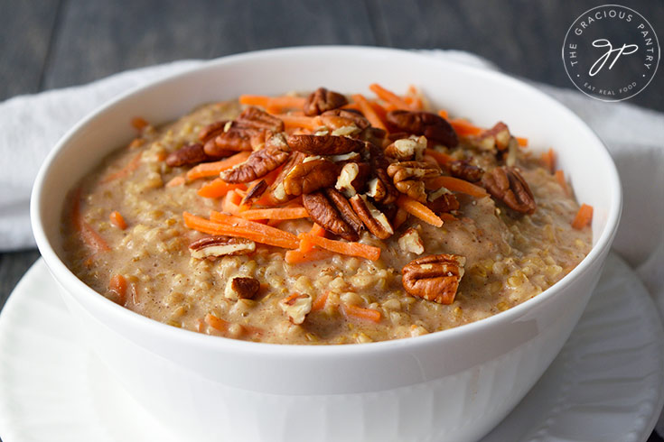 Carrot Cake Oatmeal poured into a white bowl and garnished with fresh grated carrots and chopped pecans.