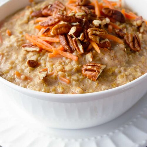 A white bowl sitting on a white plate and filled with this Carrot Cake Oatmeal Recipe.