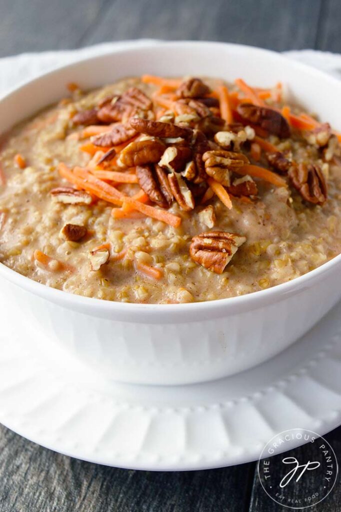 A white bowl sitting on a white plate and filled with this Carrot Cake Oatmeal Recipe.