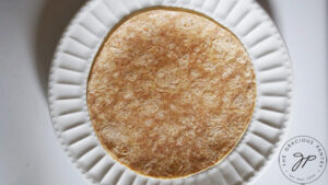 A whole-grain tortilla laid out on a white plate.
