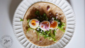 Lettuce, hard boiled eggs slices and minced onions layers on a whole grain tortilla.
