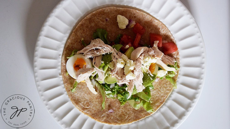 Tomatoes, avocado, chicken and blue cheese crumbles layered on top of hard boiled egg and lettuce on a whole-grain tortilla.