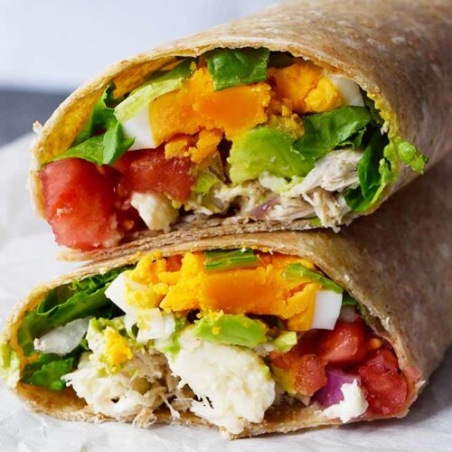A front view of a cut Cobb Salad Wrap laying on a piece of parchment.