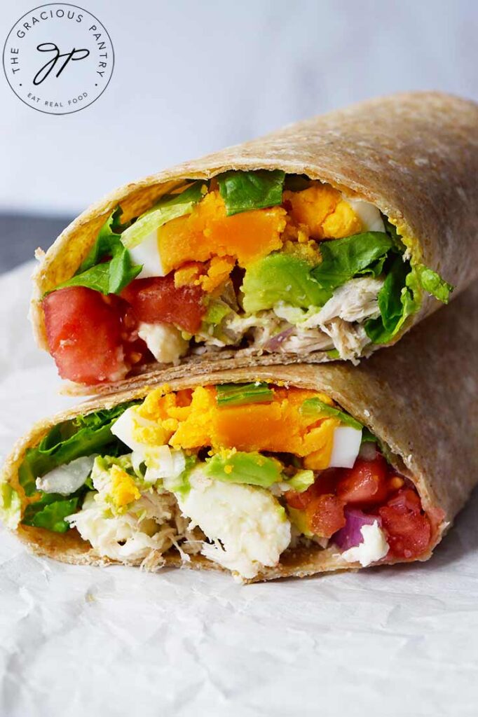 A front view of a cut Cobb Salad Wrap laying on a piece of parchment.