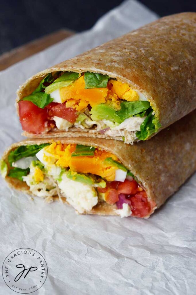 A side view of a cut Cobb Salad Wrap, stacked up on a piece of parchment paper.