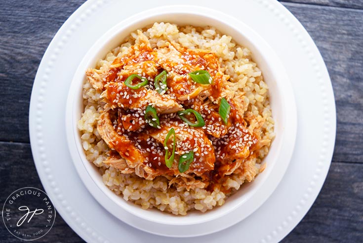 A white bowl filled with this Crock Pot Honey Sesame Chicken and garnished with sesame seeds and green onion slices.
