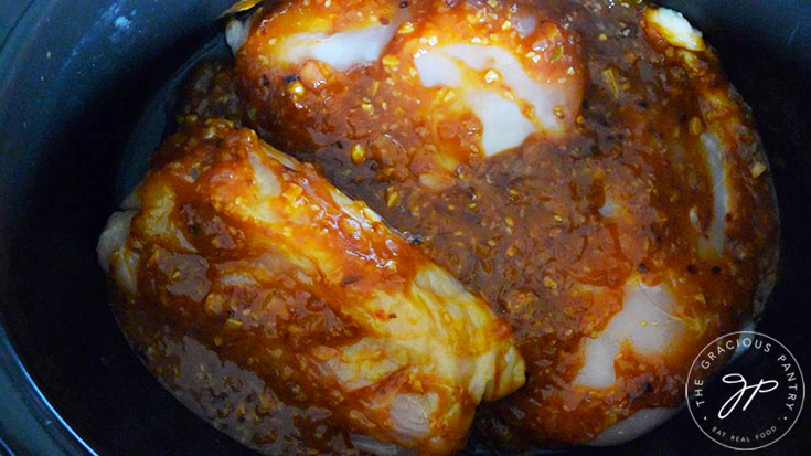 Three chicken breasts in a slow cooker crock with honey sesame sauce poured over the top.