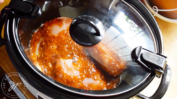 Chicken with honey sesame sauce in a crock pot with a lid over the top.