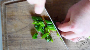 Slicing a green onion on a wooden cutting board.