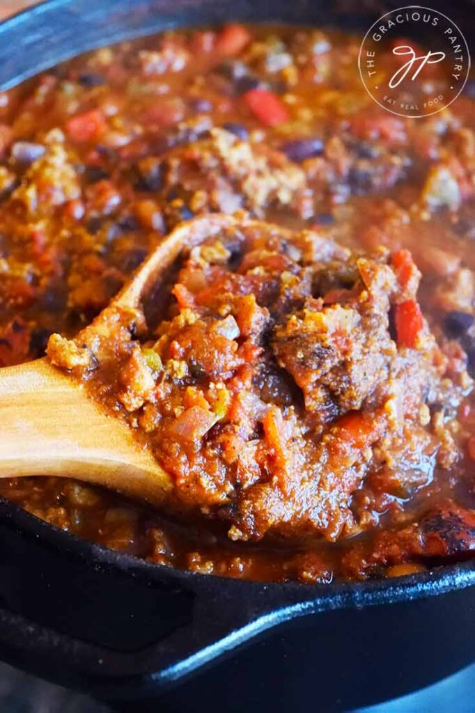 A wooden spoon lifts a spoonful of Dutch Oven Chili out of a cast iron dutch oven.